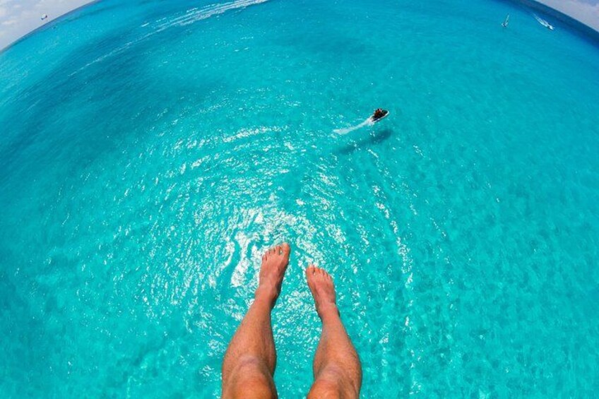 Une paire de jambes dans une piscine d’eau d’un bleu cristallin, avec une personne qui nage au loin. 2