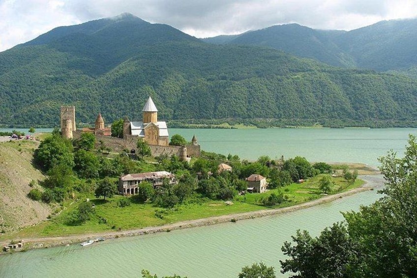 A historic church complex by a calm lake surrounded by lush green hills. 1