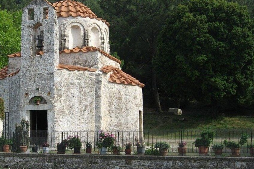 Una iglesia blanca con un campanario, rodeada por una cerca y macetas con plantas. 4