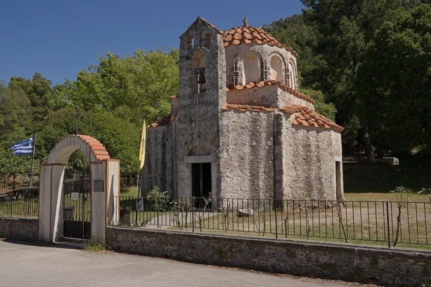 Una pequeña iglesia de piedra con un campanario, rodeada por una cerca y árboles. 5