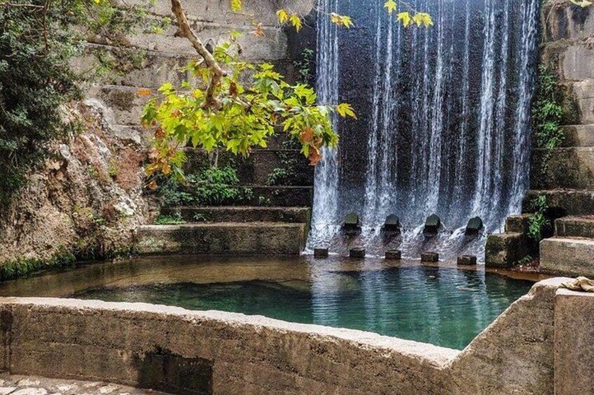A waterfall cascading over stone steps into a pool, surrounded by greenery and stone walls. 2