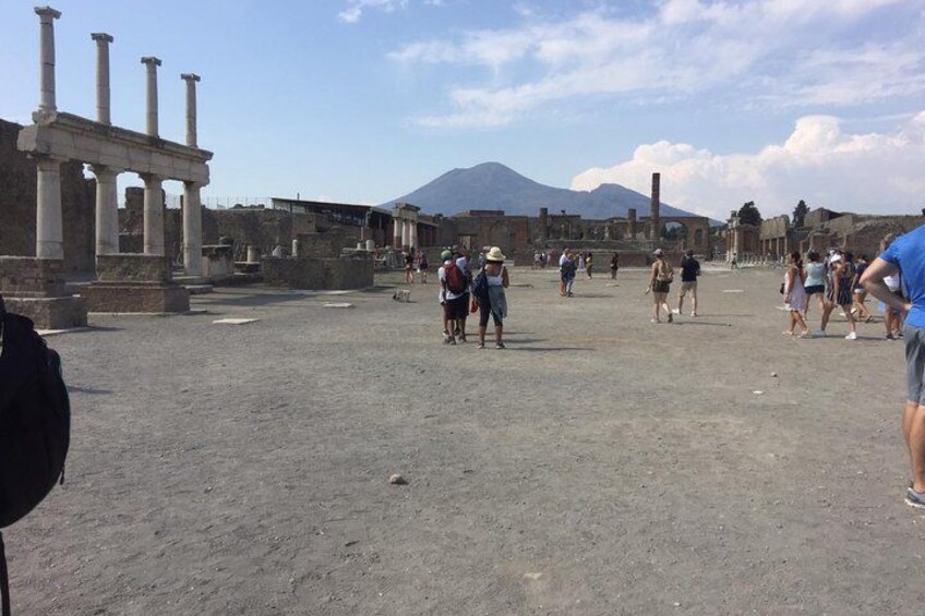 Ancient ruins with columns, a volcano in the background, and people walking. 3