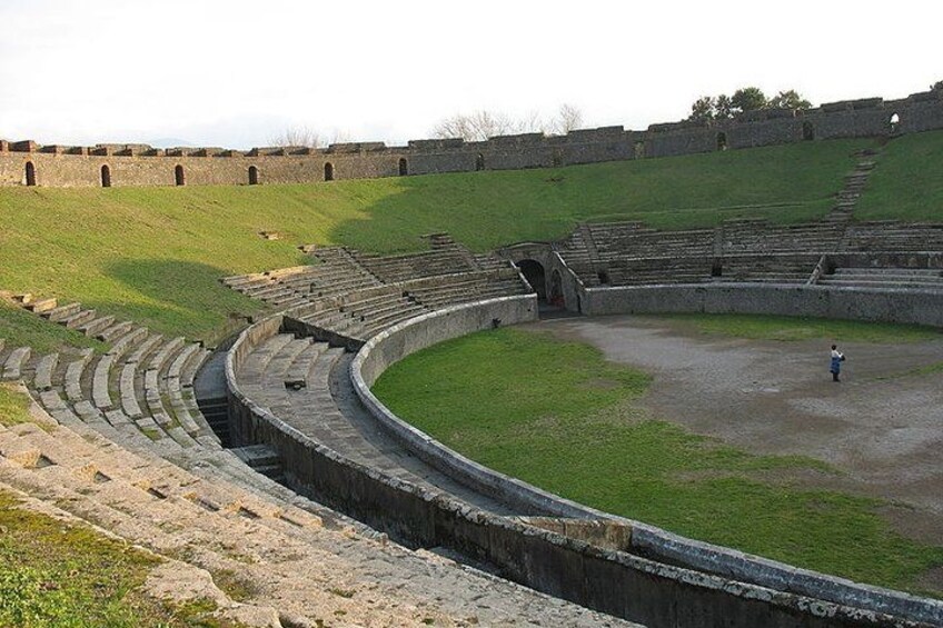 An ancient amphitheater with stone seating and a grassy hill. 2