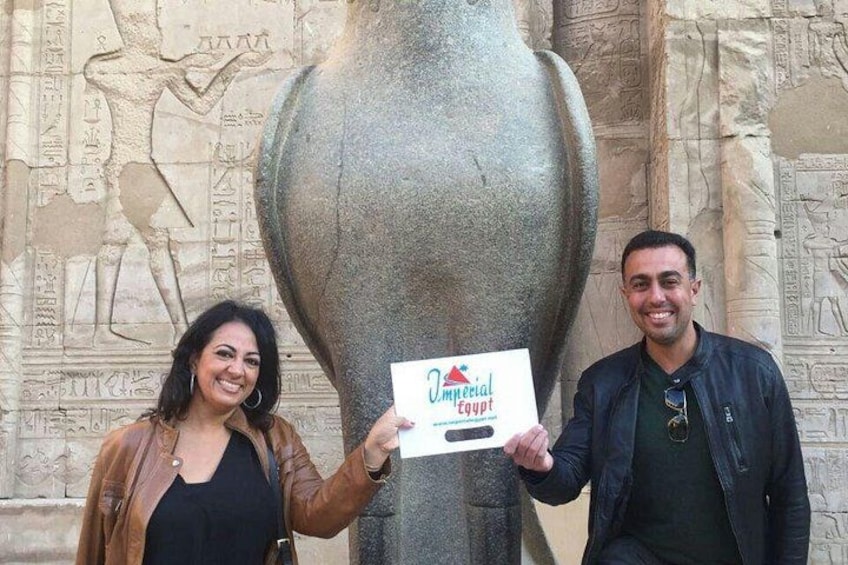 Two people holding a sign in front of a large stone structure with hieroglyphs. 2