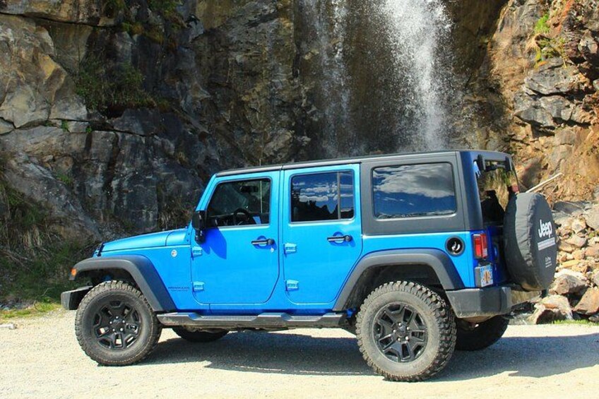 Un Jeep bleu est garé devant une cascade. 1