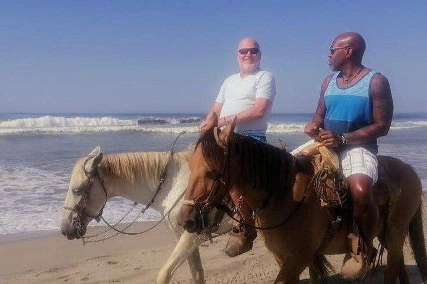 Two people riding horses on a beach with ocean waves in the background. 3