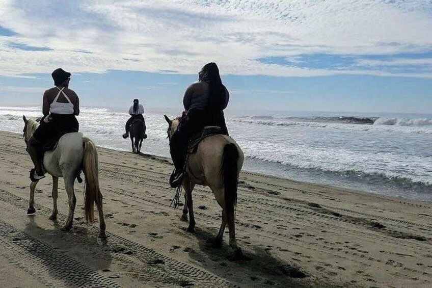 People riding horses on a beach with ocean waves in the background. 5
