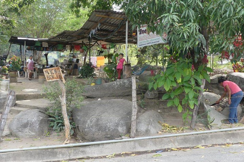 Escena de mercado con un letrero, un árbol y una persona trabajando cerca de rocas. 3