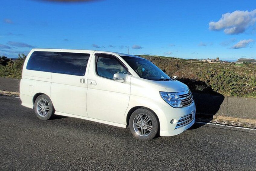 Una camioneta blanca estacionada en una carretera, con cielo azul despejado y una colina distante al fondo. 5