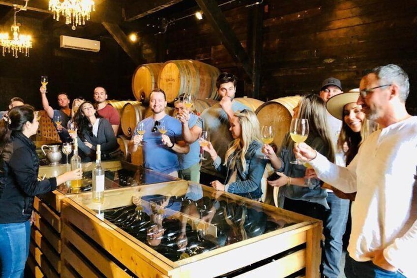 A group of people toasting with wine glasses in a rustic cellar with wooden barrels in the background. 1