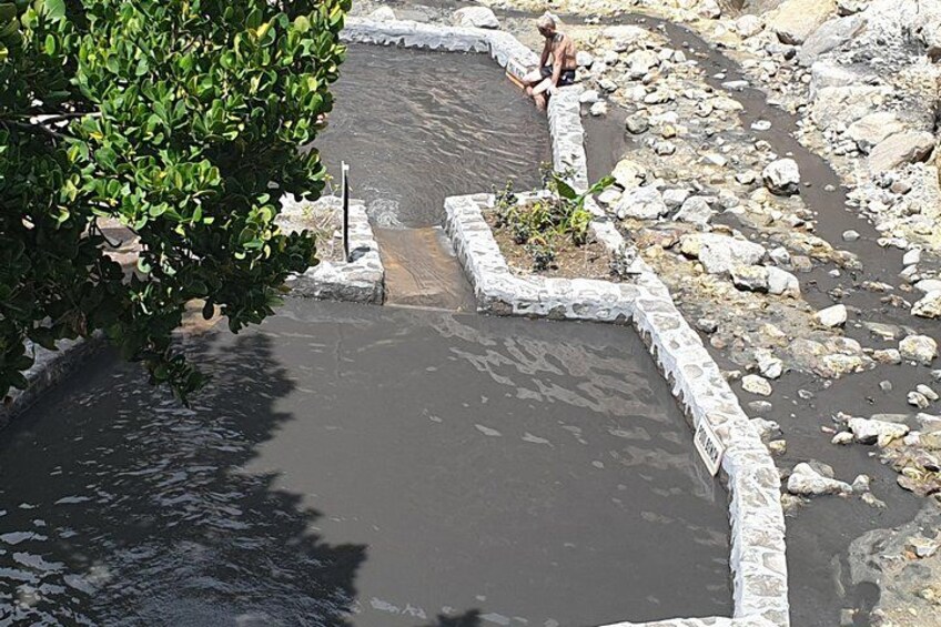 A man sitting by a small pond surrounded by rocks and greenery. 1