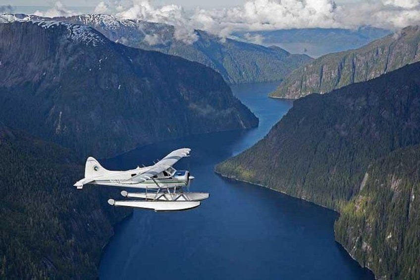 A seaplane flying over a fjord surrounded by mountains. 2