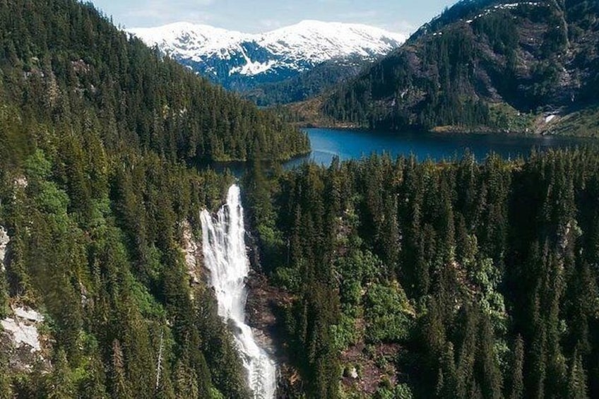 A waterfall, dense forest, and a lake with mountains in the background. 4