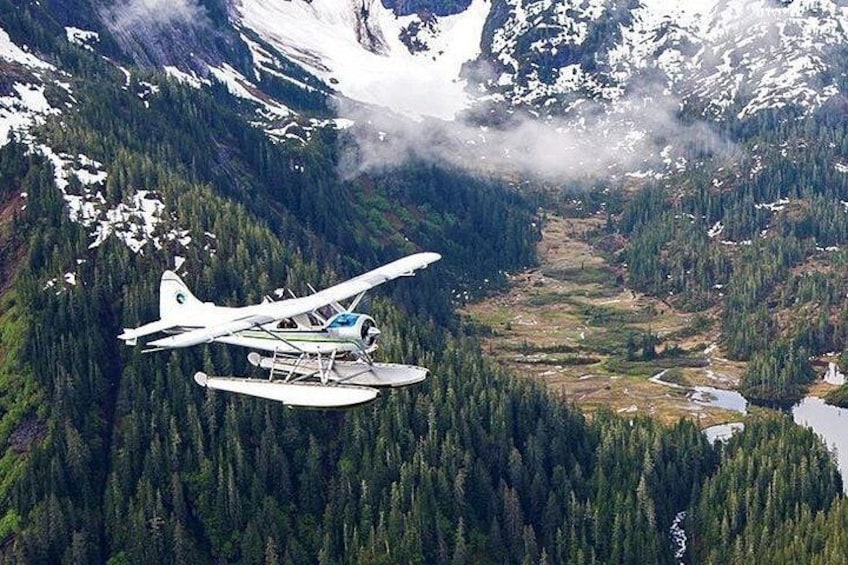 A seaplane flying over a mountainous area with dense forests and a river. 5