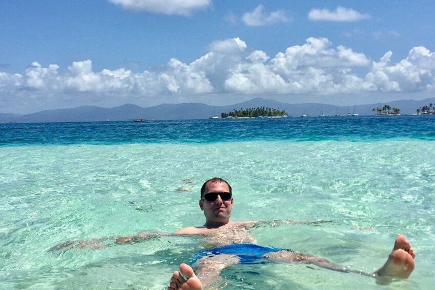 Una persona flotando en aguas turquesas cristalinas, con un paisaje montañoso al fondo. 1