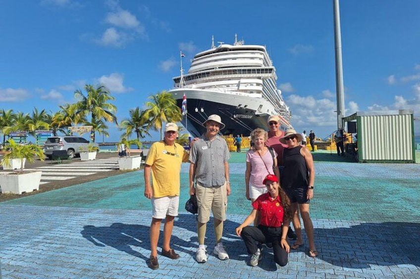 Un groupe de personnes posant devant un navire de croisière, avec des palmiers et un ciel bleu clair en arrière-plan. 4