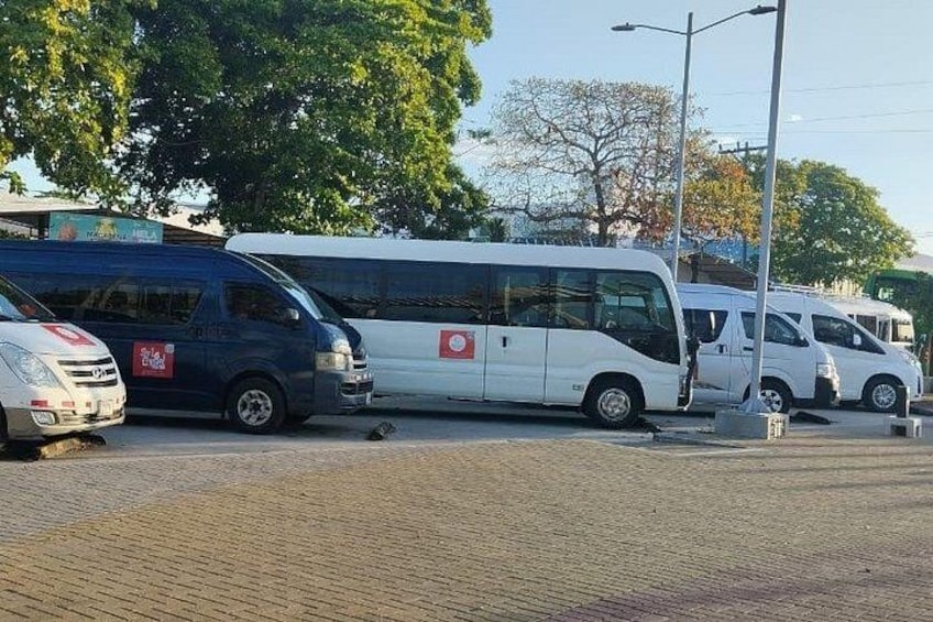 A parking lot with several white and blue vans, a white bus, and a white car. 3