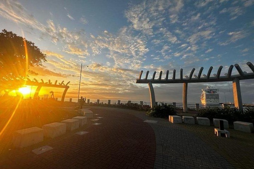 A sunset over a waterfront promenade with a metal structure and a cruise ship in the background. 2