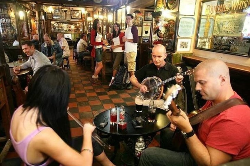 Eine Bar mit sitzenden und stehenden Personen, ein Mann spielt Banjo, und eine Frau hält ein Getränk. 2