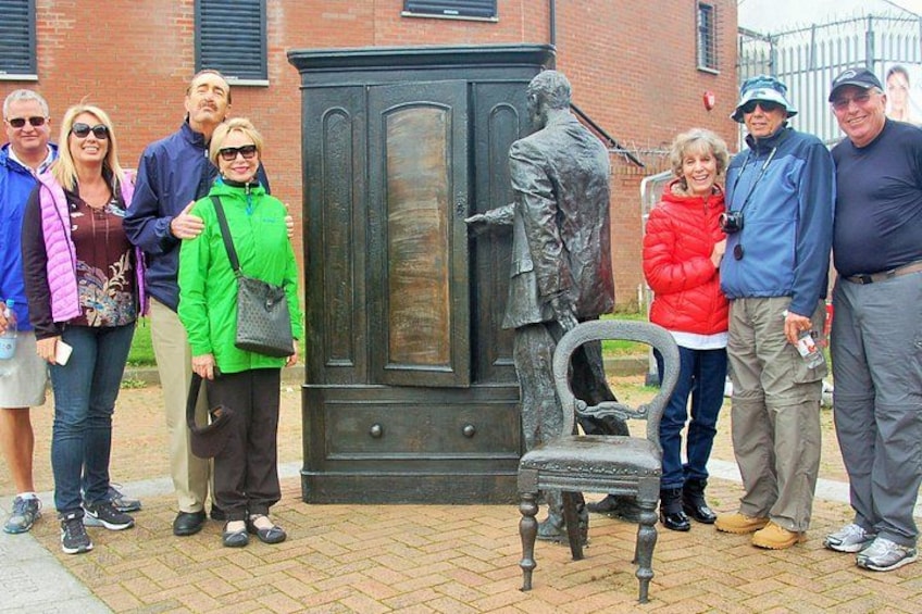 Eine Gruppe von Menschen steht vor einer Statue und einer Bank. 1