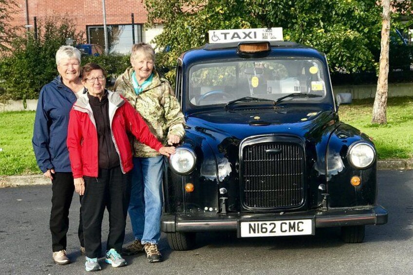 Un taxi nero d'epoca con il simbolo per l'accessibilità ai disabili, parcheggiato in strada con tre persone nelle vicinanze. 1