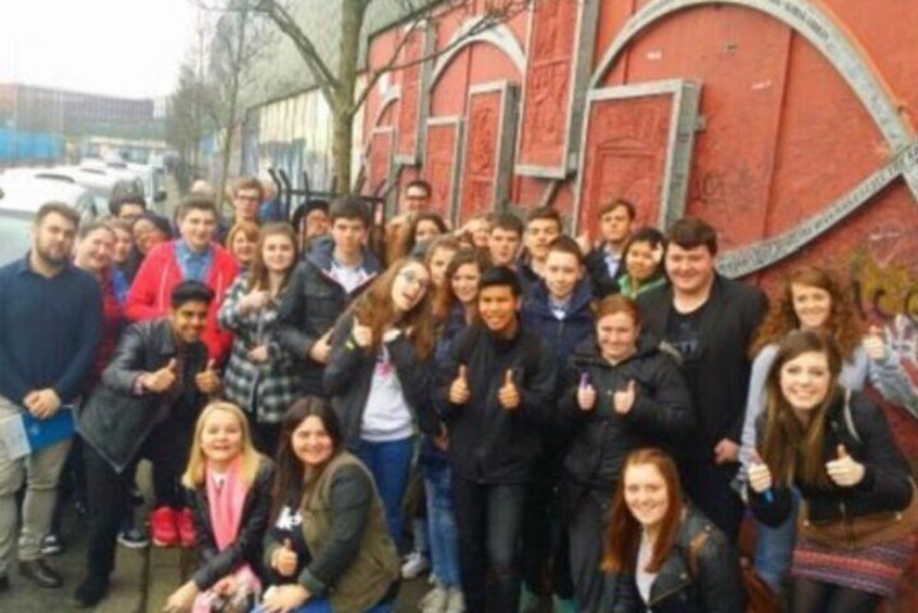 A group of people posing in front of a red building with graffiti. 4