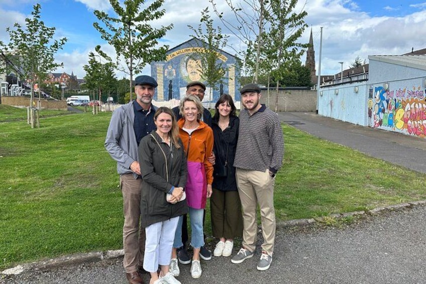 A group of people standing in front of a mural with text and a building in the background. 2