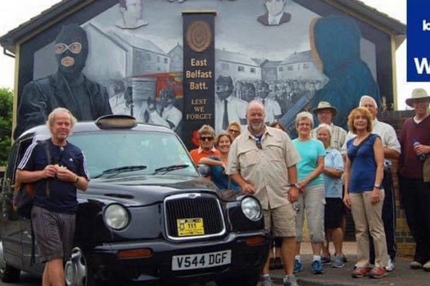 A group of people standing in front of a mural with a car in the foreground. 3
