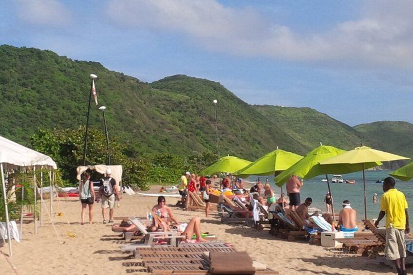 Una playa con gente tomando el sol bajo sombrillas, una carpa y montañas al fondo. 4