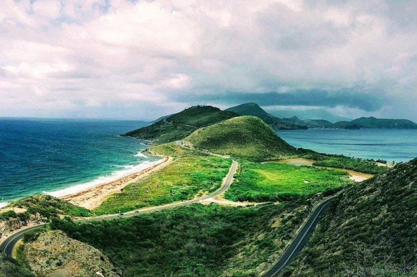A coastal landscape with a beach, a winding road, and rolling hills. 1