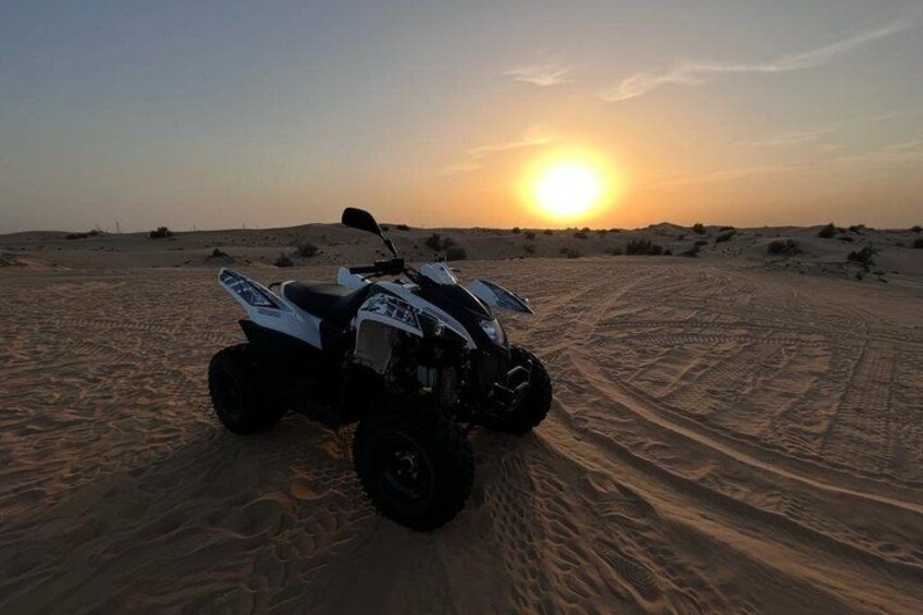 Un cuatrimoto estacionado en un sendero arenoso del desierto, con el sol poniéndose al fondo. 3