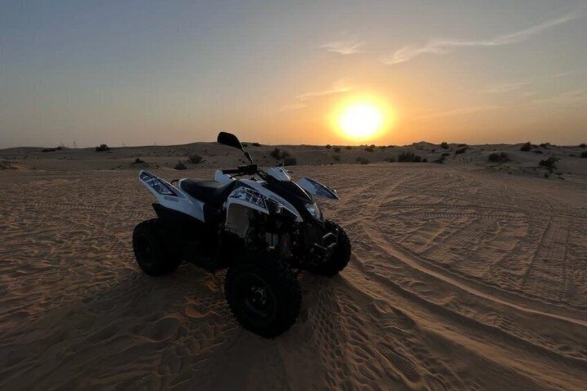 Un cuatrimoto estacionado en un sendero arenoso del desierto, con el sol poniéndose al fondo. 4
