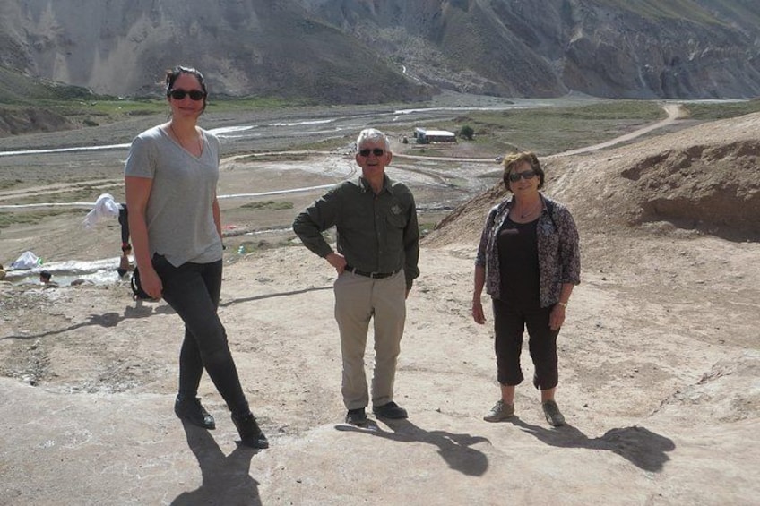 Three people standing on a rocky terrain with a mountainous background. 1