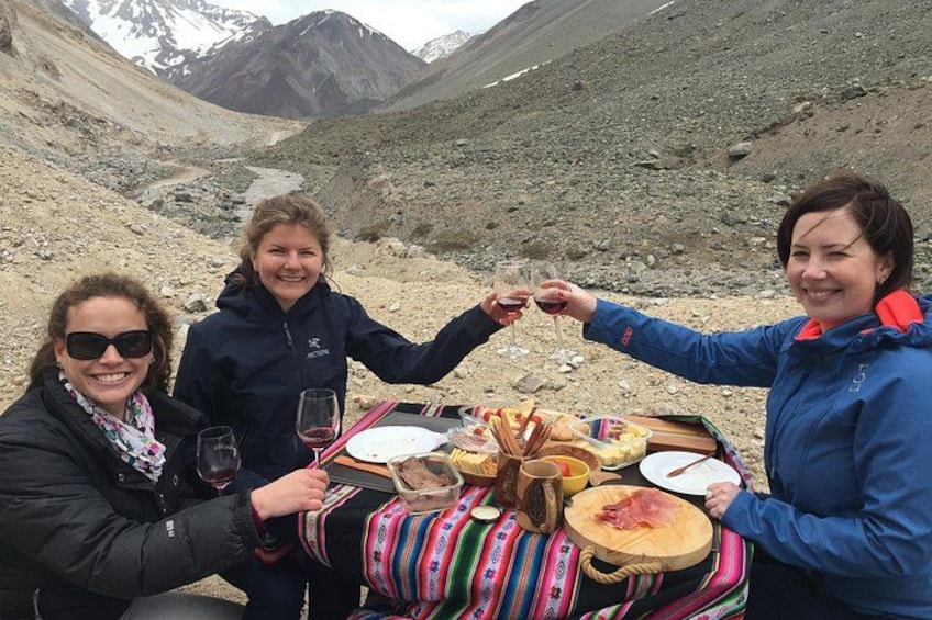Three people toasting with wine glasses at a table with a meal, outdoors with a mountainous backdrop. 1