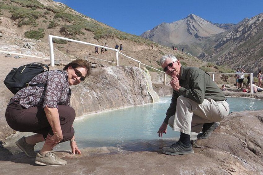 Two people near a natural hot spring with a mountainous backdrop. 4