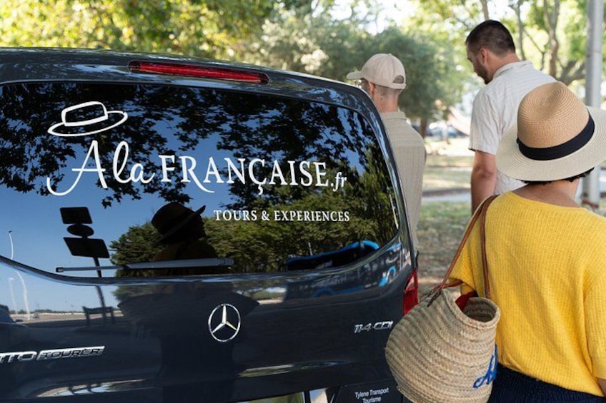A black car with a logo and text on the back window, parked outdoors with people standing nearby. 2