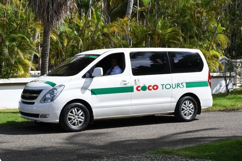 A white van with green and red branding parked on a road with palm trees in the background. 1