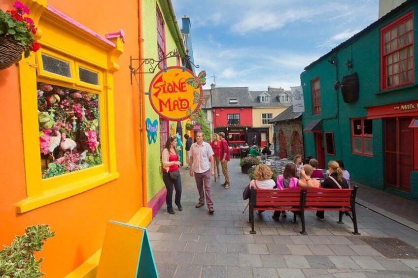 A colorful street with a sign reading 'Stone Mad,' a bench, and people walking. 2