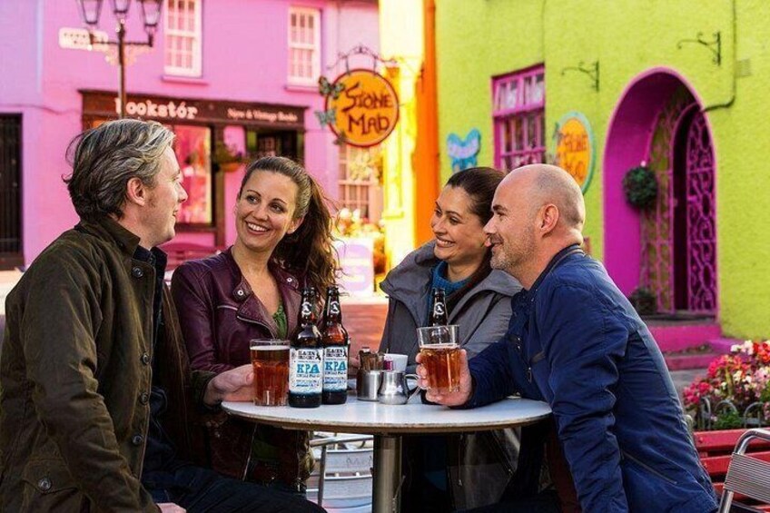 Un grupo de personas sentadas en una mesa con bebidas, un edificio colorido con un letrero que dice 'Søren Madsen' y una tienda con un letrero que dice 'Lookstør'. 4