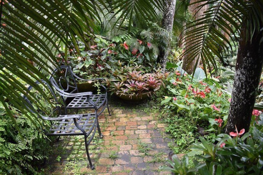 A garden with a metal bench, lush greenery, and a brick pathway. 3