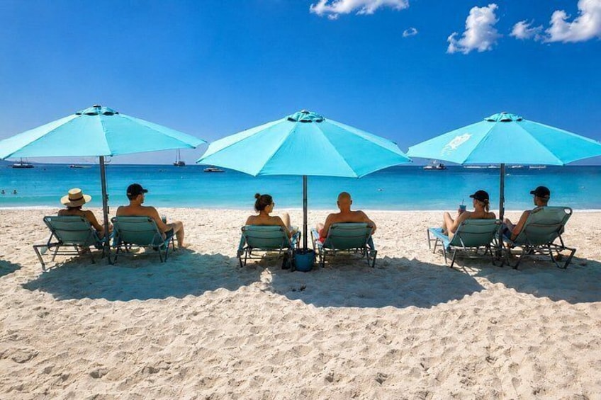 A beach with people sitting under blue umbrellas. 2