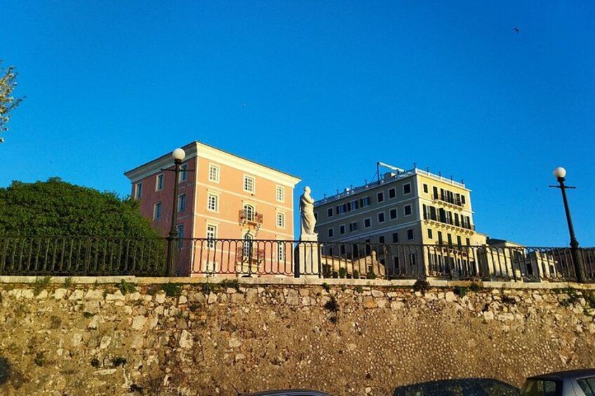 A stone wall, a pink building, and a white building with a statue in front of them. 5