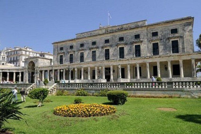 A historic building with a courtyard, a circular flower bed, and a clear sky. 1