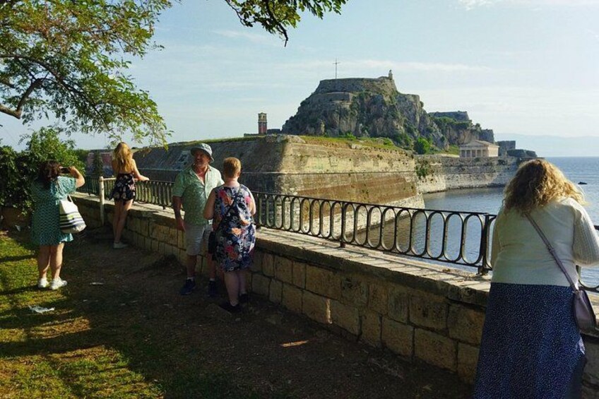A group of people standing by a stone wall overlooking a fort and the sea. 4