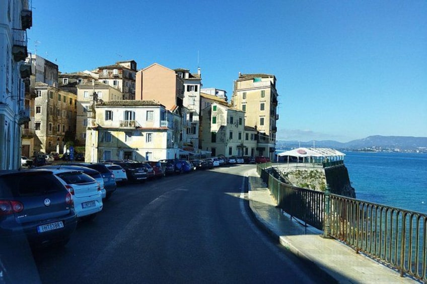 A coastal road with parked cars, buildings, and a clear blue sky. 3