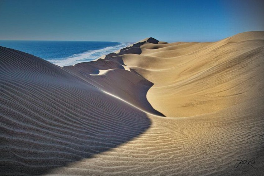 A desert landscape with sand dunes and a view of the ocean. 2
