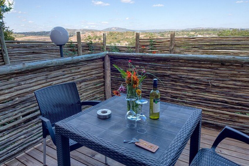 A table with chairs and bottles on a deck with a view of the countryside. 4