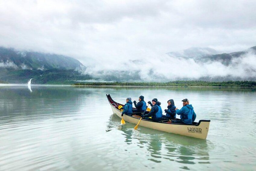 A group of people in a canoe on a calm lake with mountains in the background. 3