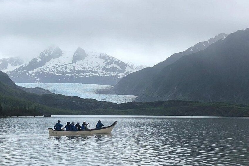 A group of people in a boat on a calm lake with mountains in the background. 3