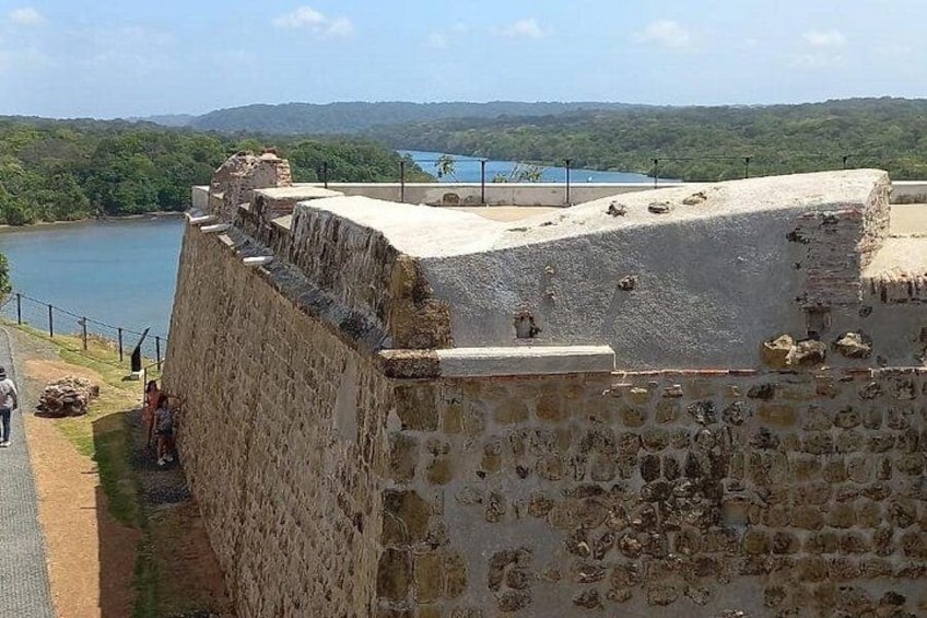 Una fortificación de piedra con vista a un cuerpo de agua, bajo un cielo despejado y colinas distantes. 2